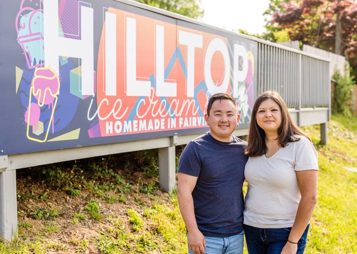 Hilltop Ice Cream Shop owners standing beside the colorful roadside shop sign